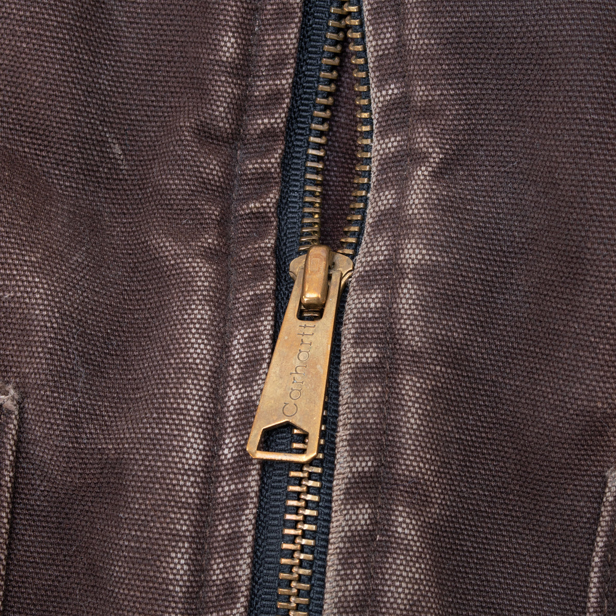 Close-up of brass-tone Carhartt zipper pull and teeth on brown fabric