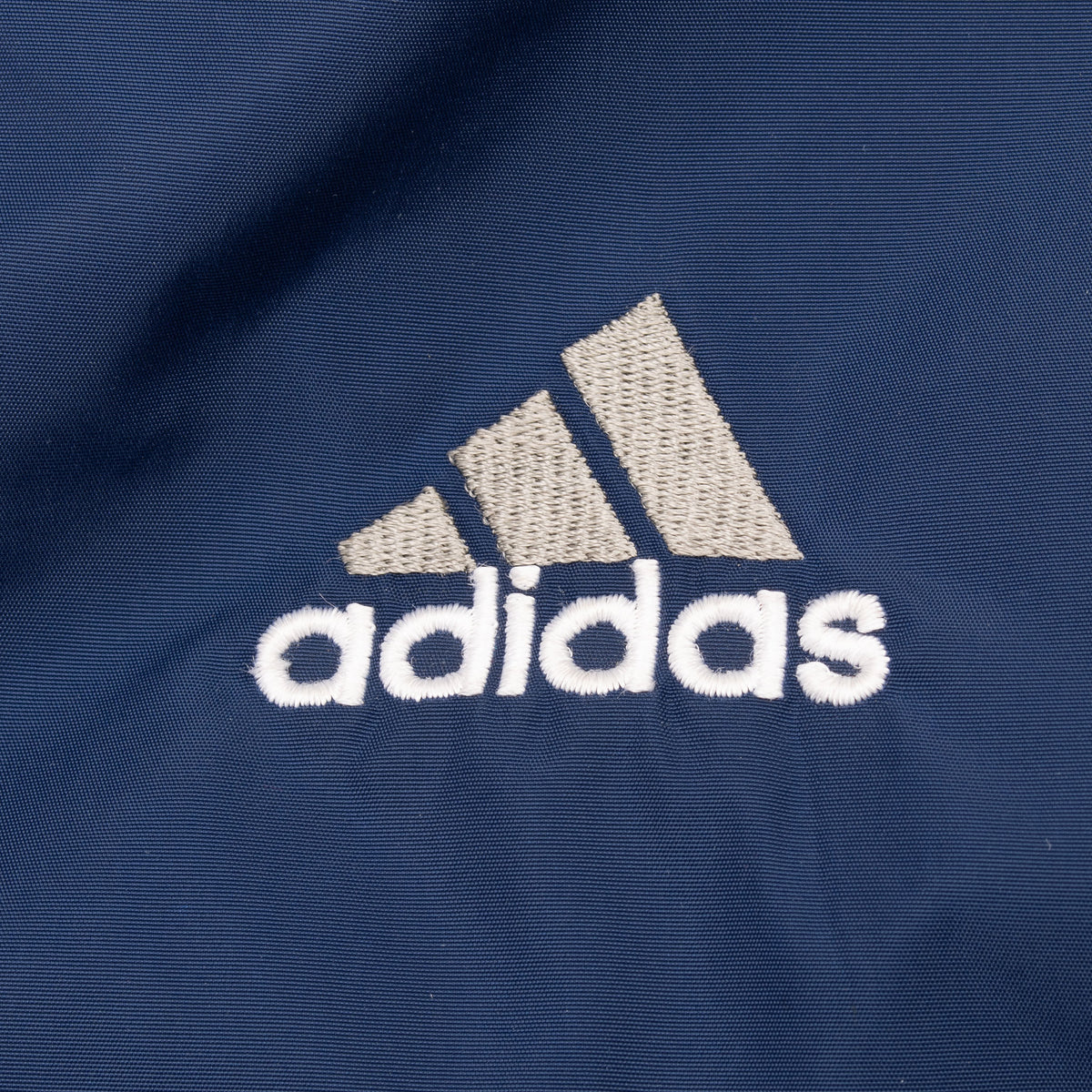 Close-up of small white and gray Adidas chest embroidery on blue fabric