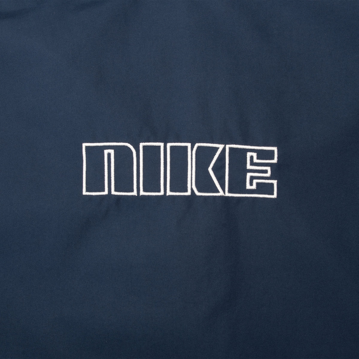 Close-up of outlined Nike embroidery on back of navy windbreaker