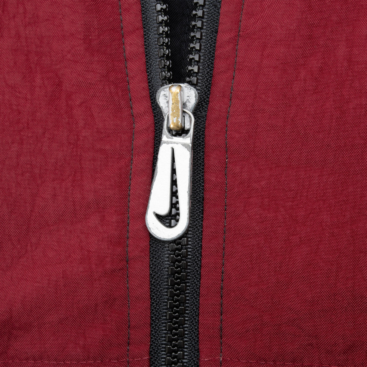 Close-up of Nike Swoosh zipper pull on burgundy jacket fabric