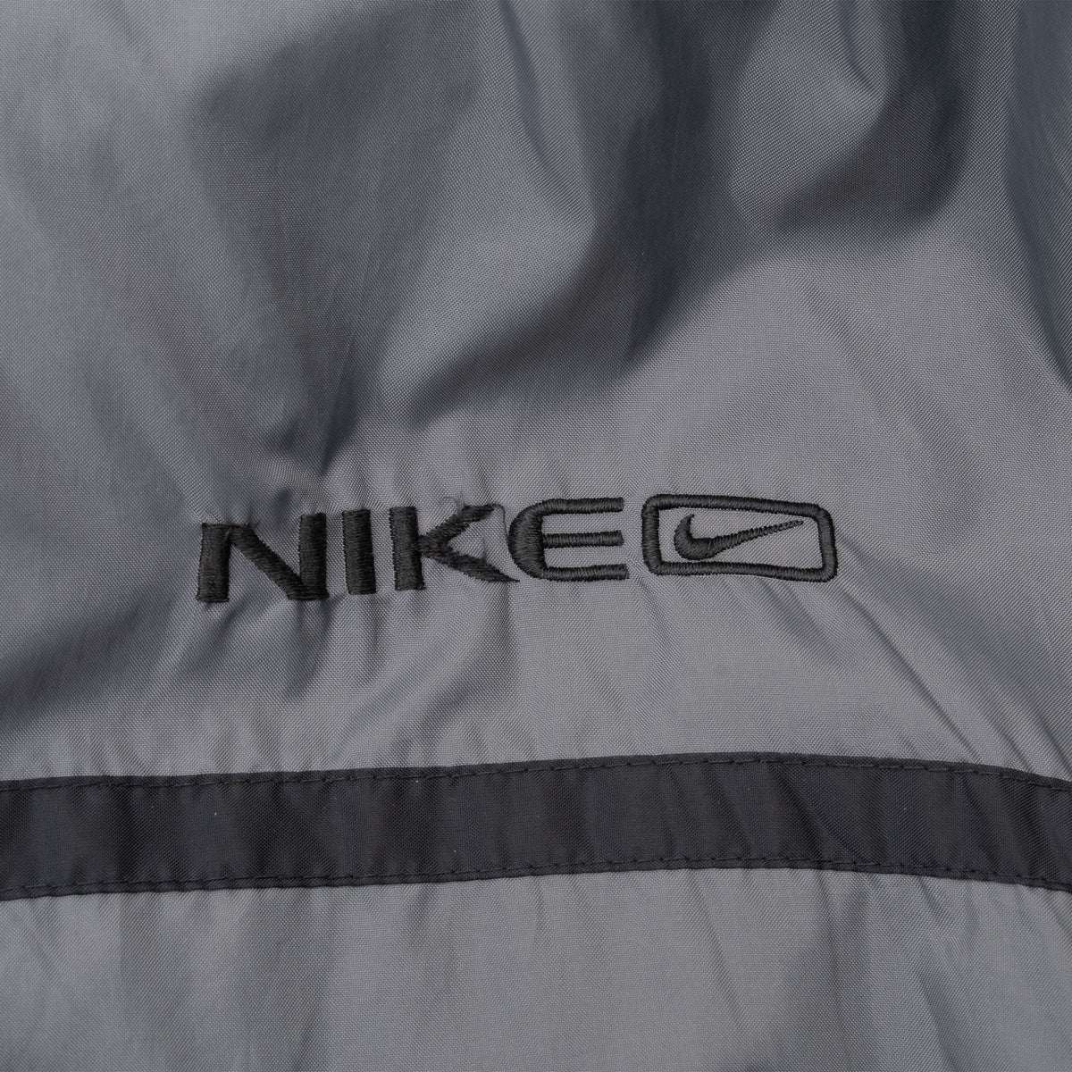 Close-up of black Nike logo embroidery on grey windbreaker chest
