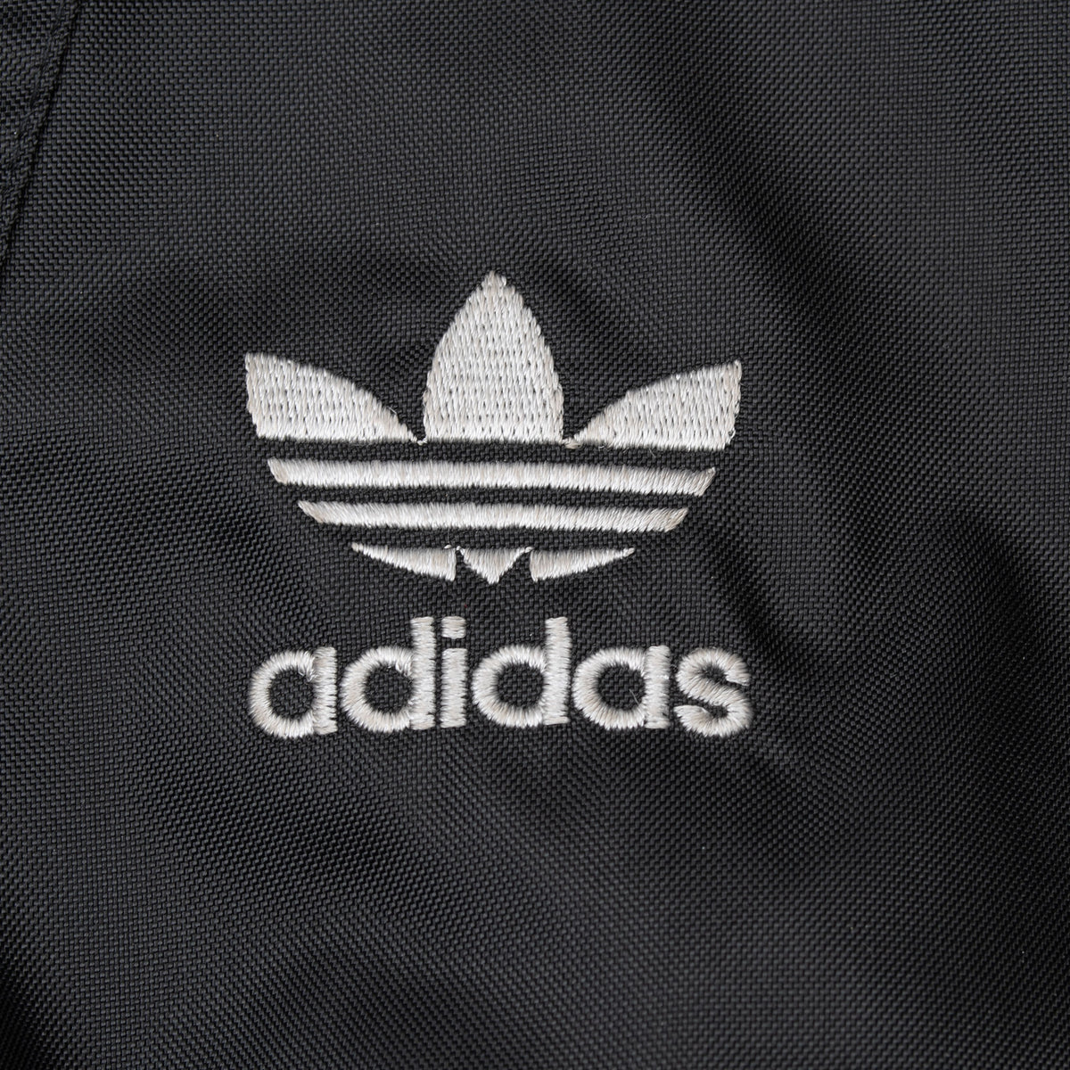 Close-up of white Adidas Trefoil embroidery on black fabric