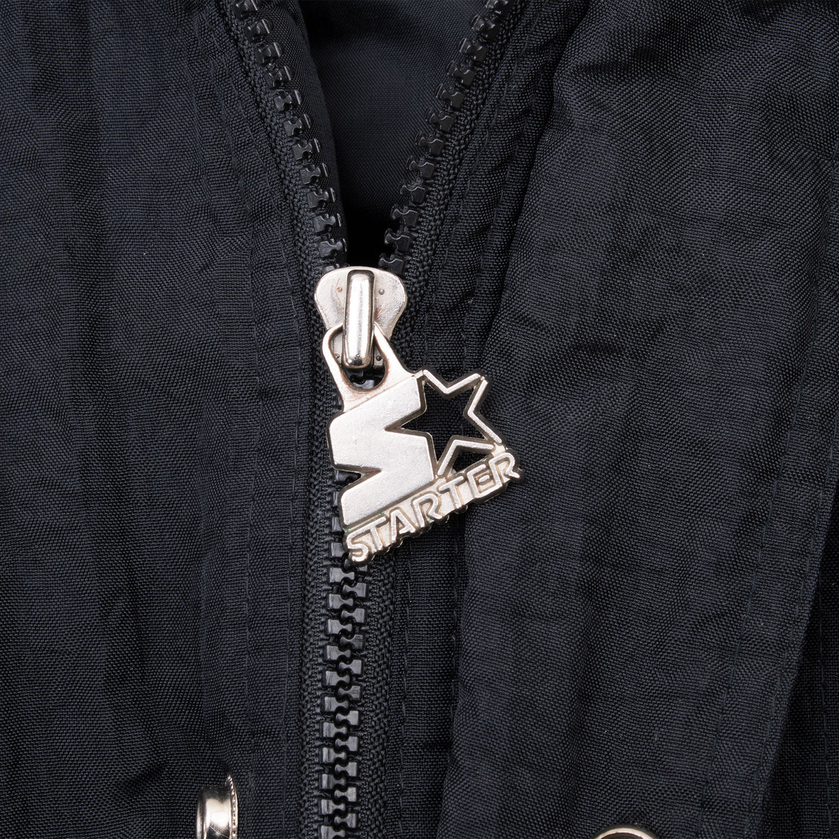 Close-up of silver Starter logo zipper pull on black jacket