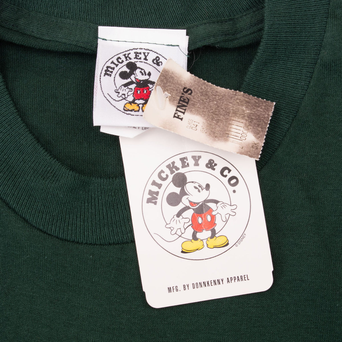 Close-up of Mickey & Co. neck label and hangtags on dark green T-shirt