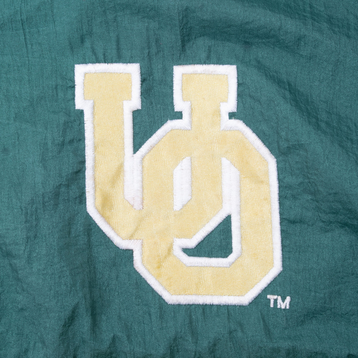 Close-up of yellow and white interlocking UO logo embroidered on green windbreaker