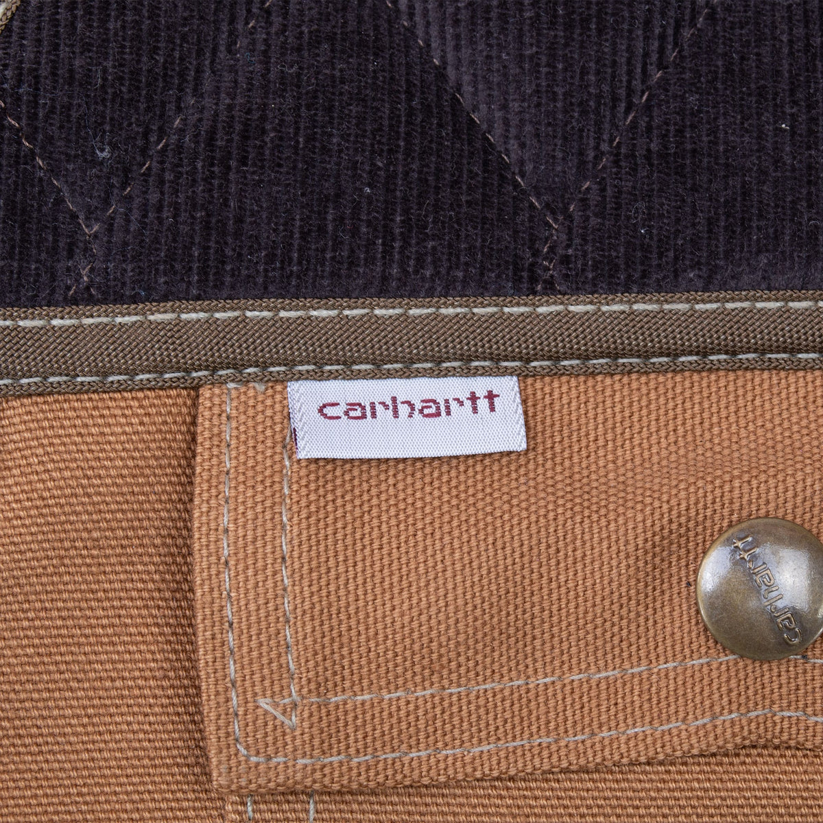 Close-up of Carhartt fabric tab, branded snap and dark quilted shoulder panel