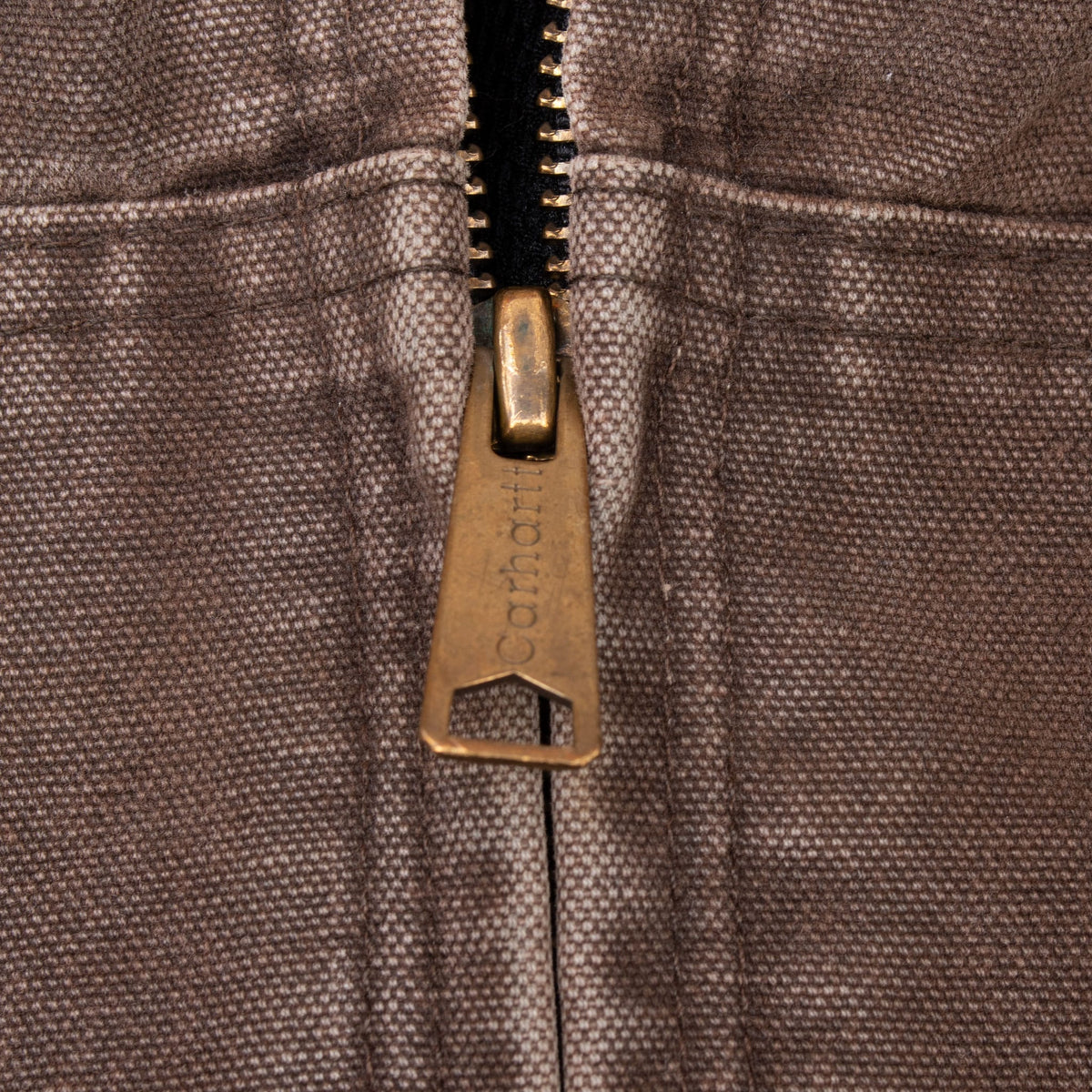 Close-up of Carhartt-branded metal zipper pull and brown fabric