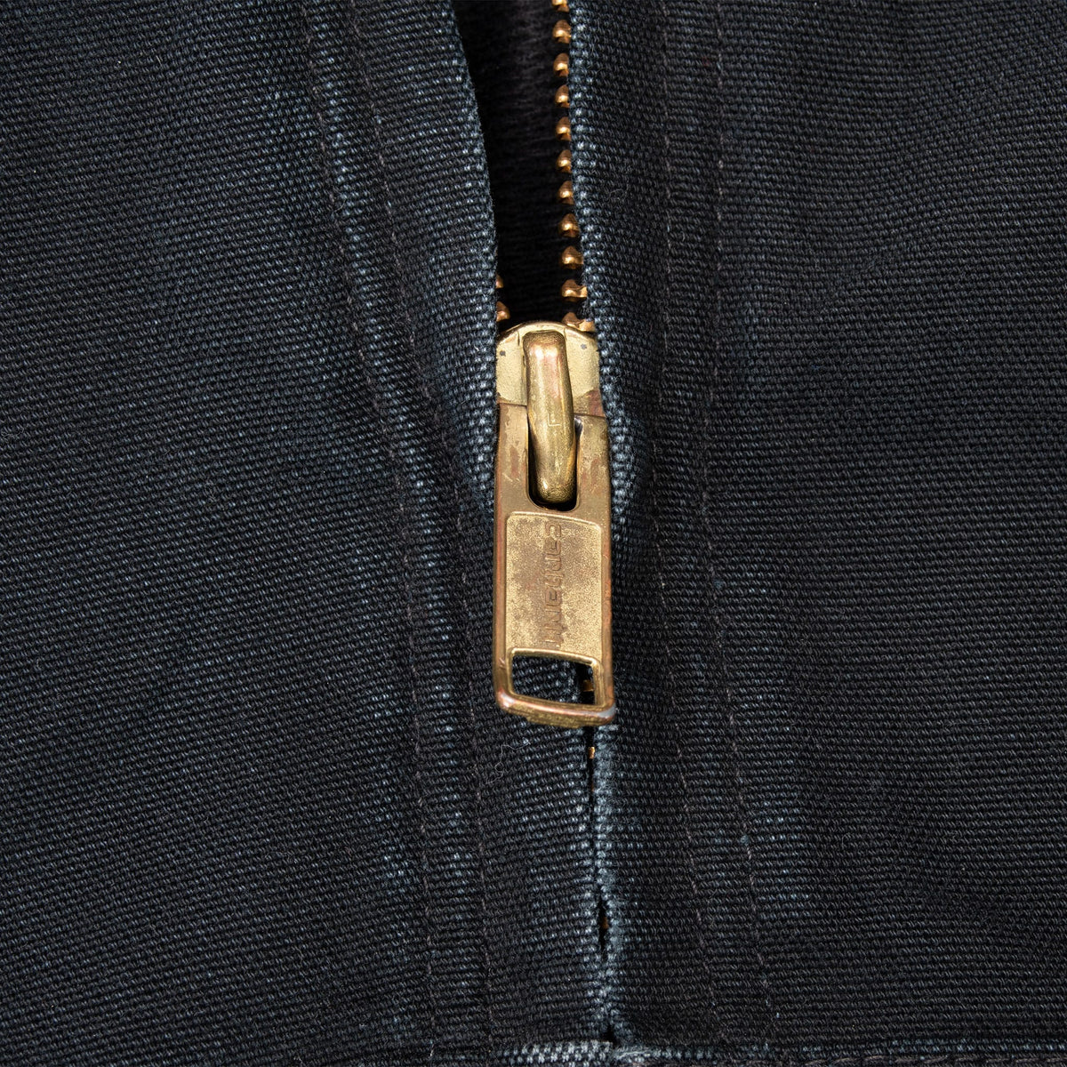 Close-up of brass-tone front zipper on black Carhartt jacket