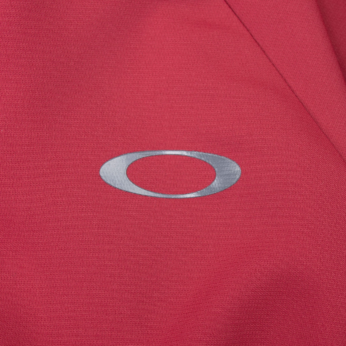 Close-up of gray Oakley ellipse chest logo on burgundy windbreaker
