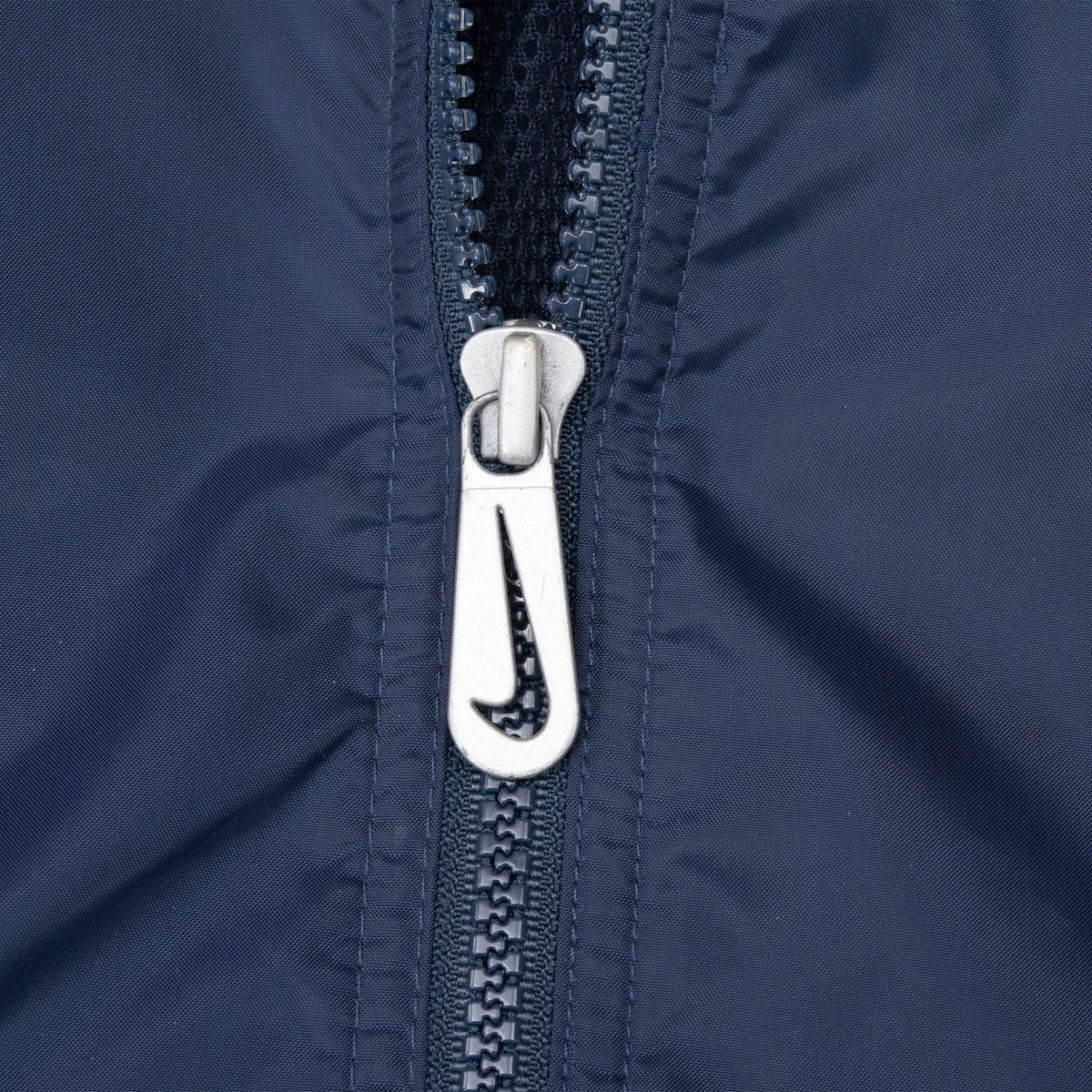 Close-up of silver Nike Swoosh cutout zipper pull on navy windbreaker