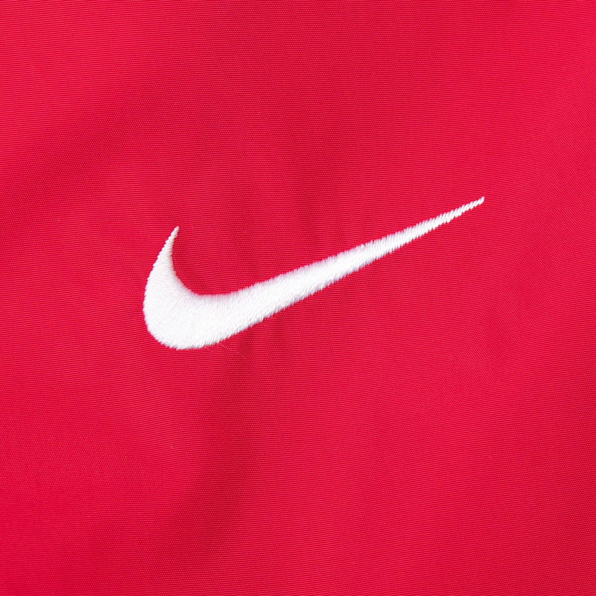 Close-up of white embroidered Nike Swoosh on red windbreaker fabric