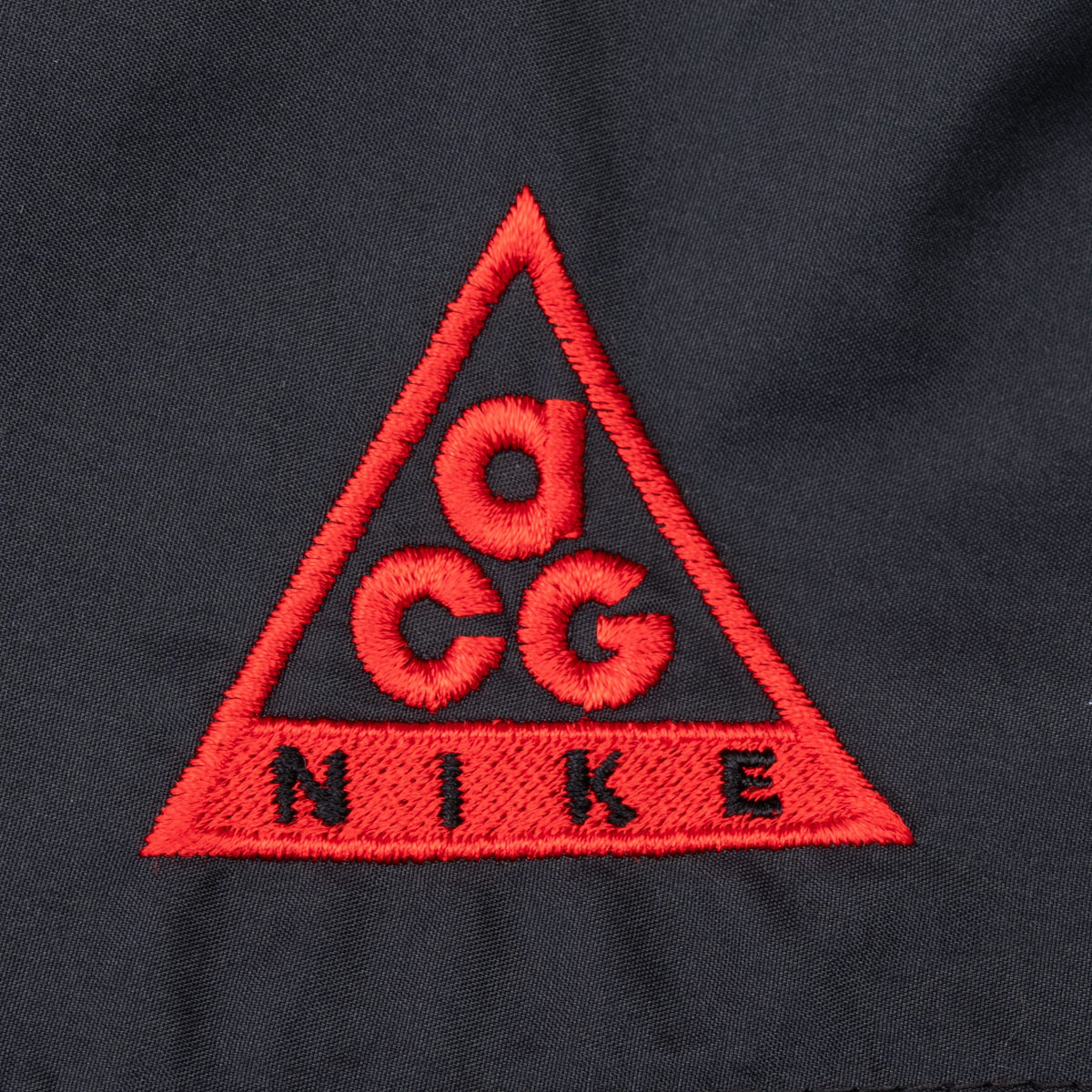 Close-up of red embroidered Nike ACG triangle logo on black fabric