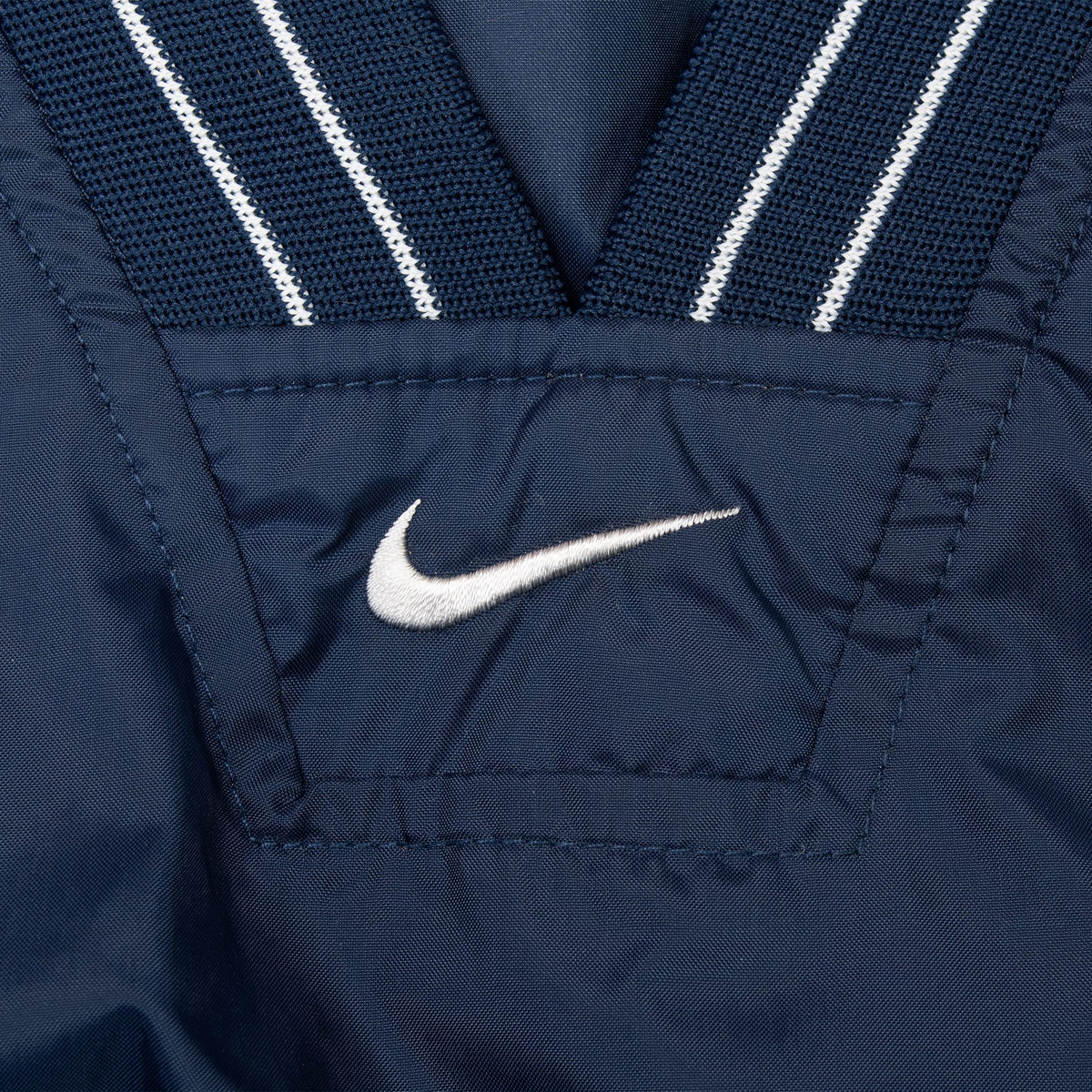 Close-up of white embroidered Nike Swoosh below the navy and white striped V-neck collar