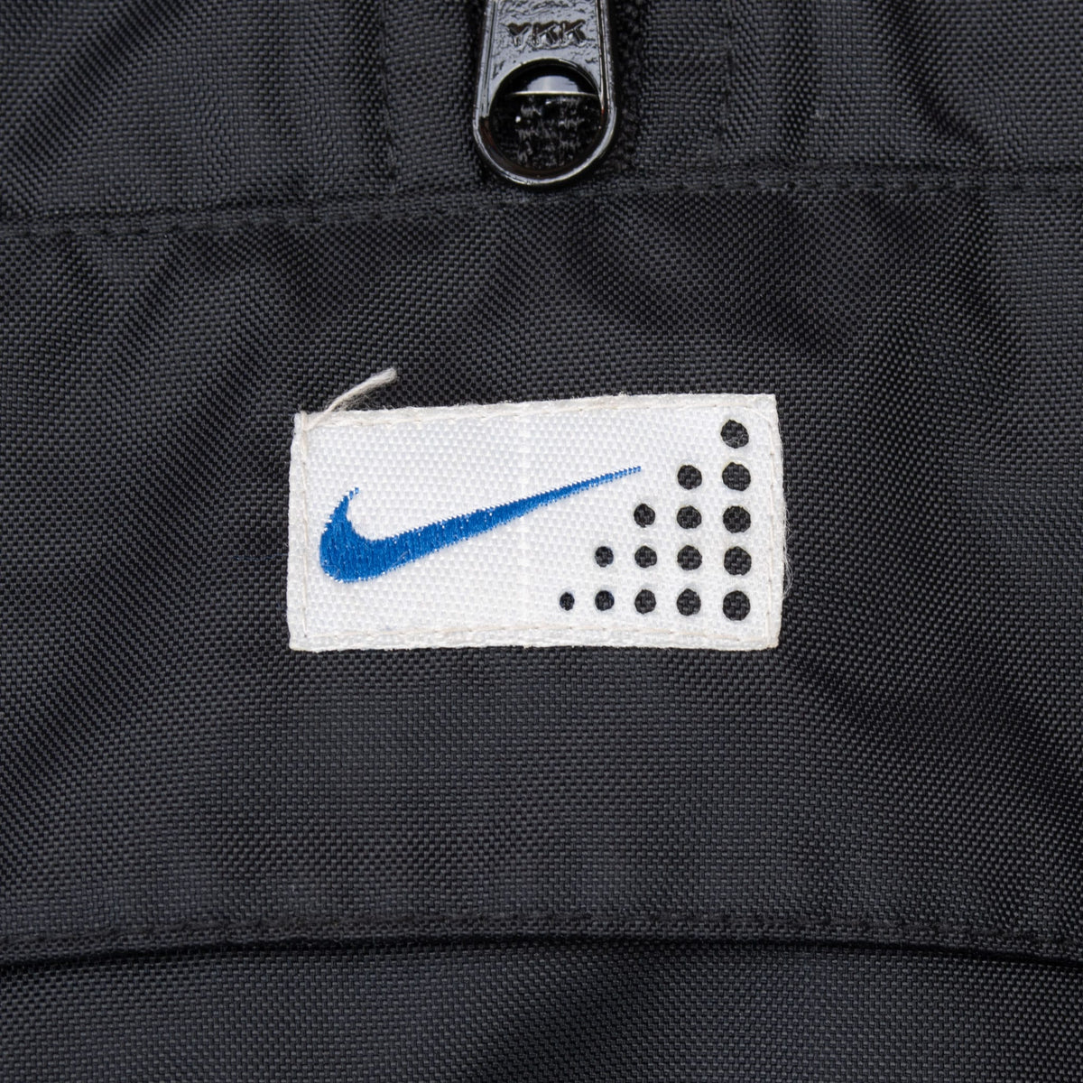 Close-up of centered white chest patch with blue Nike Swoosh and black dot graphic