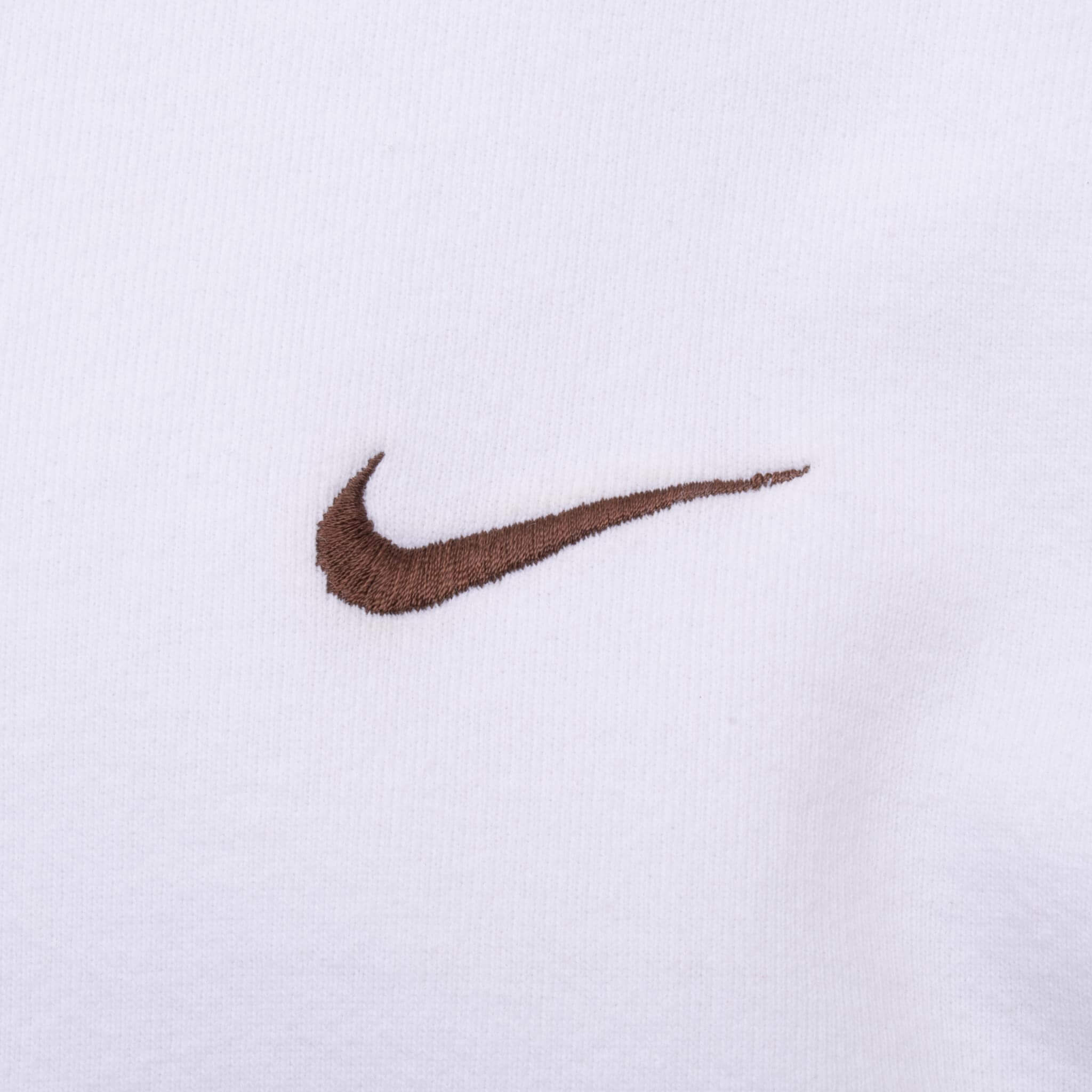 Close-up of brown Nike Swoosh embroidery on white fabric