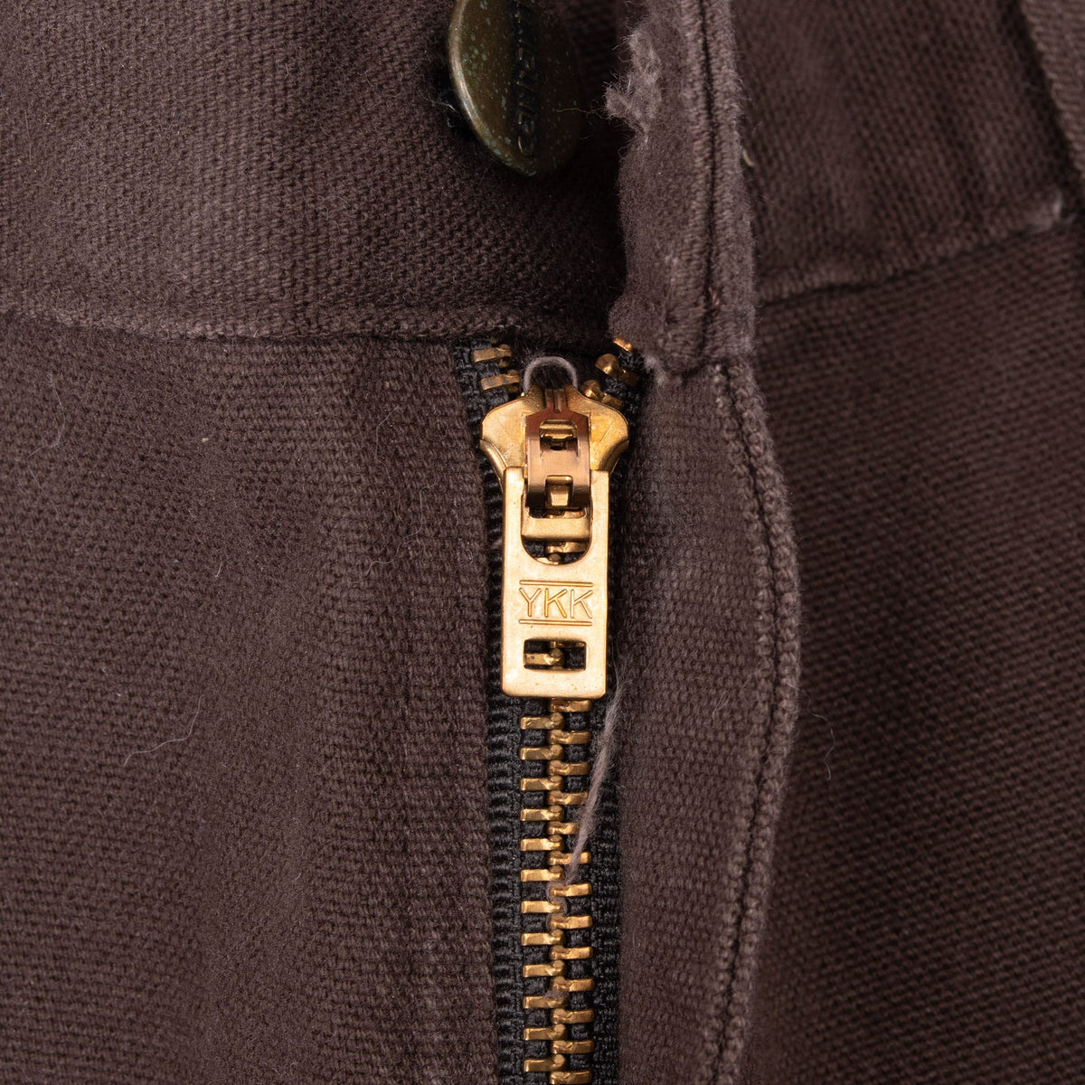 Close-up of the brass-tone YKK zip fly on dark brown Carhartt carpenter pants