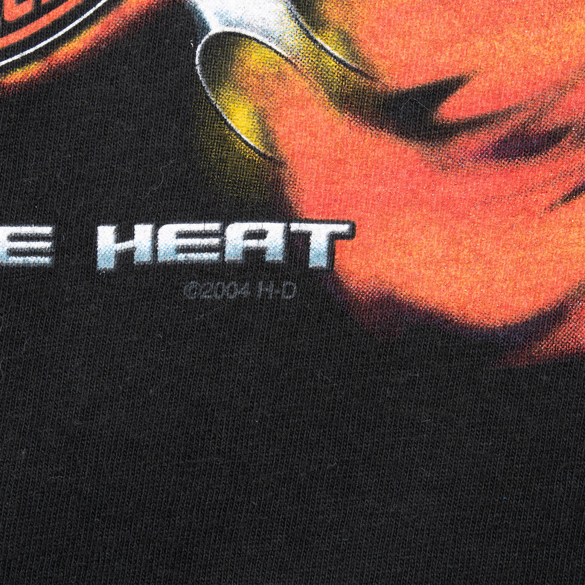 Detail of the Feel the Heat front print showing an orange flame and small 2004 copyright text