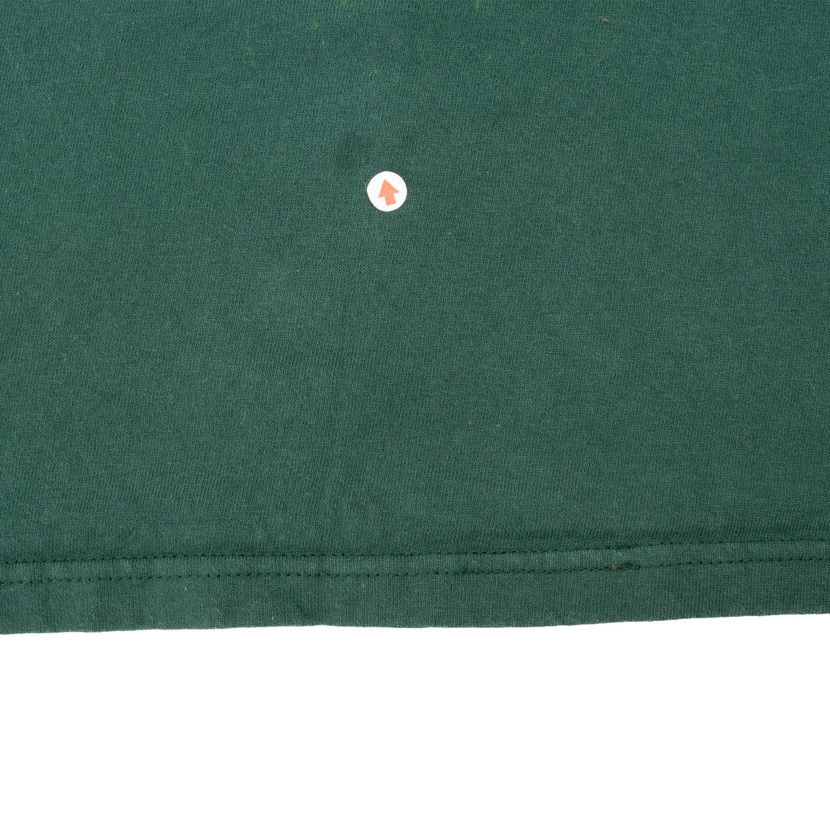 Close-up of small hole in green fabric near the bottom hem, marked with an arrow