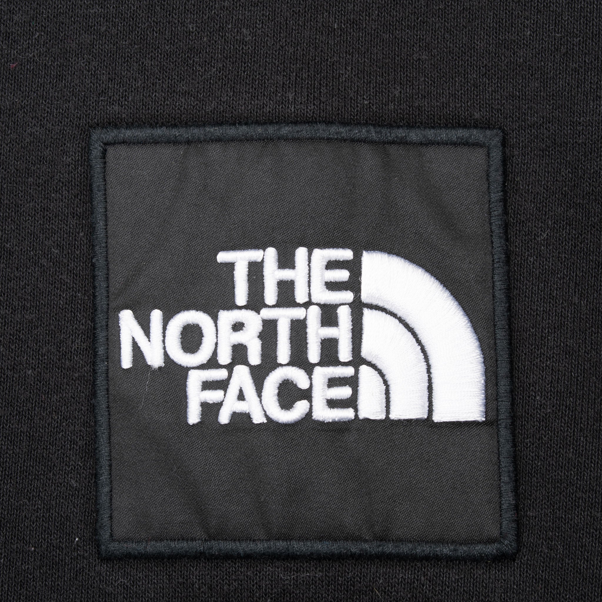 Close-up of white The North Face logo embroidered on black chest patch