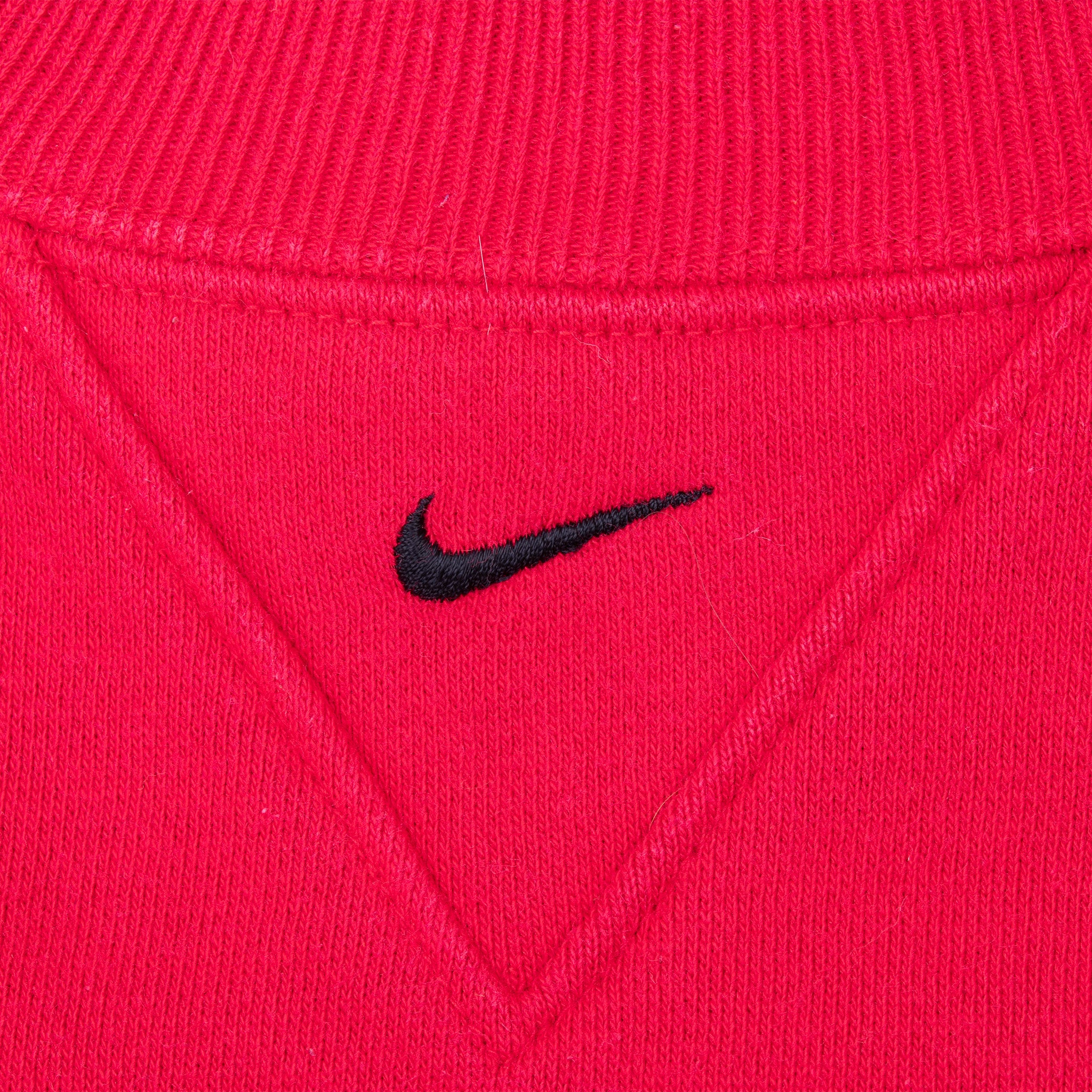 Black Nike Swoosh embroidery below the ribbed collar on red sweatshirt