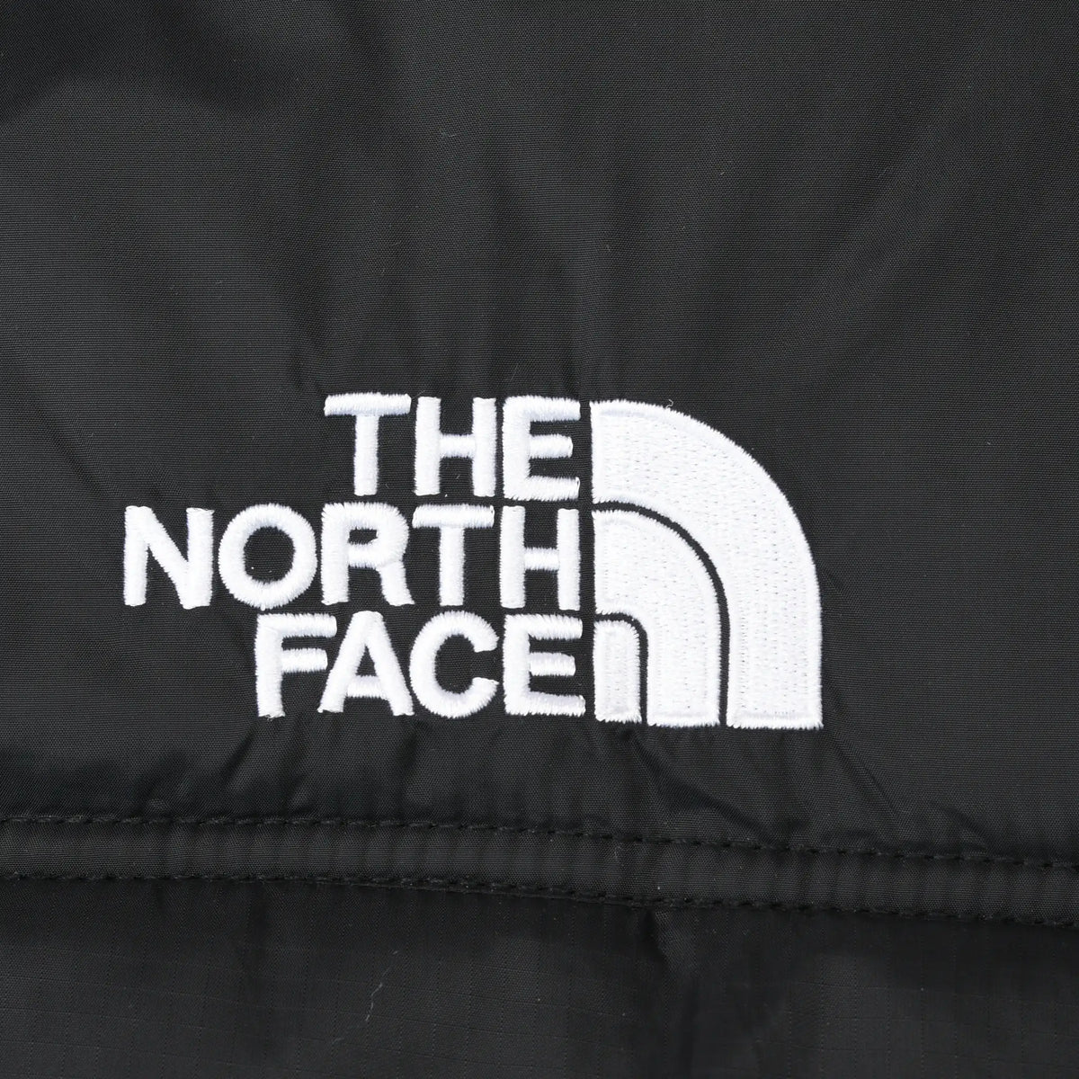 Close-up of white The North Face logo embroidery on black jacket shell