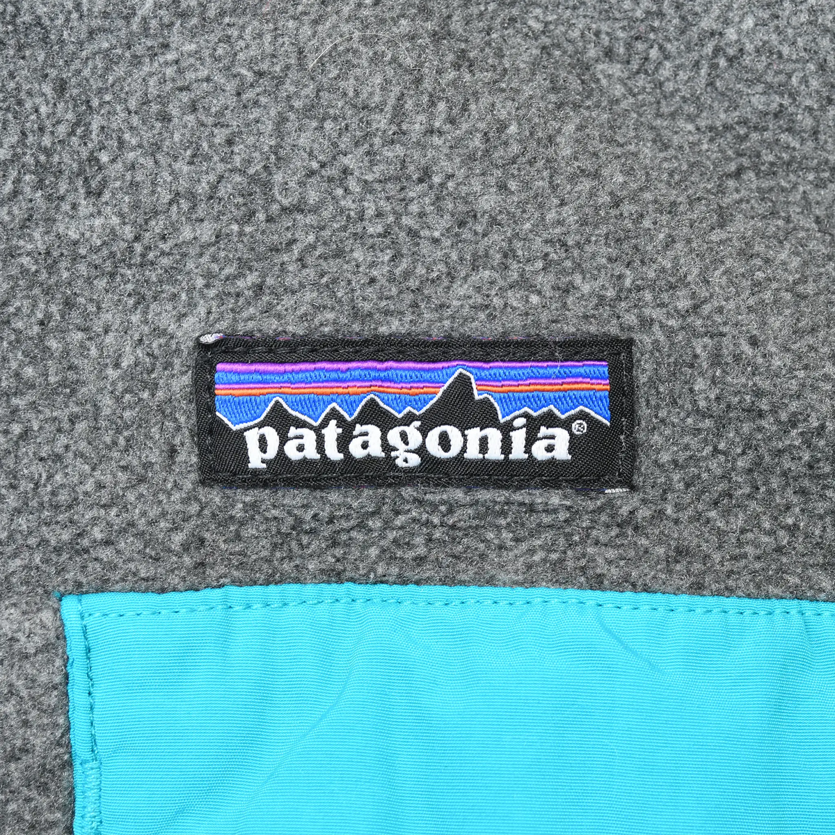 Patagonia logo above turquoise chest pocket on dark grey fleece