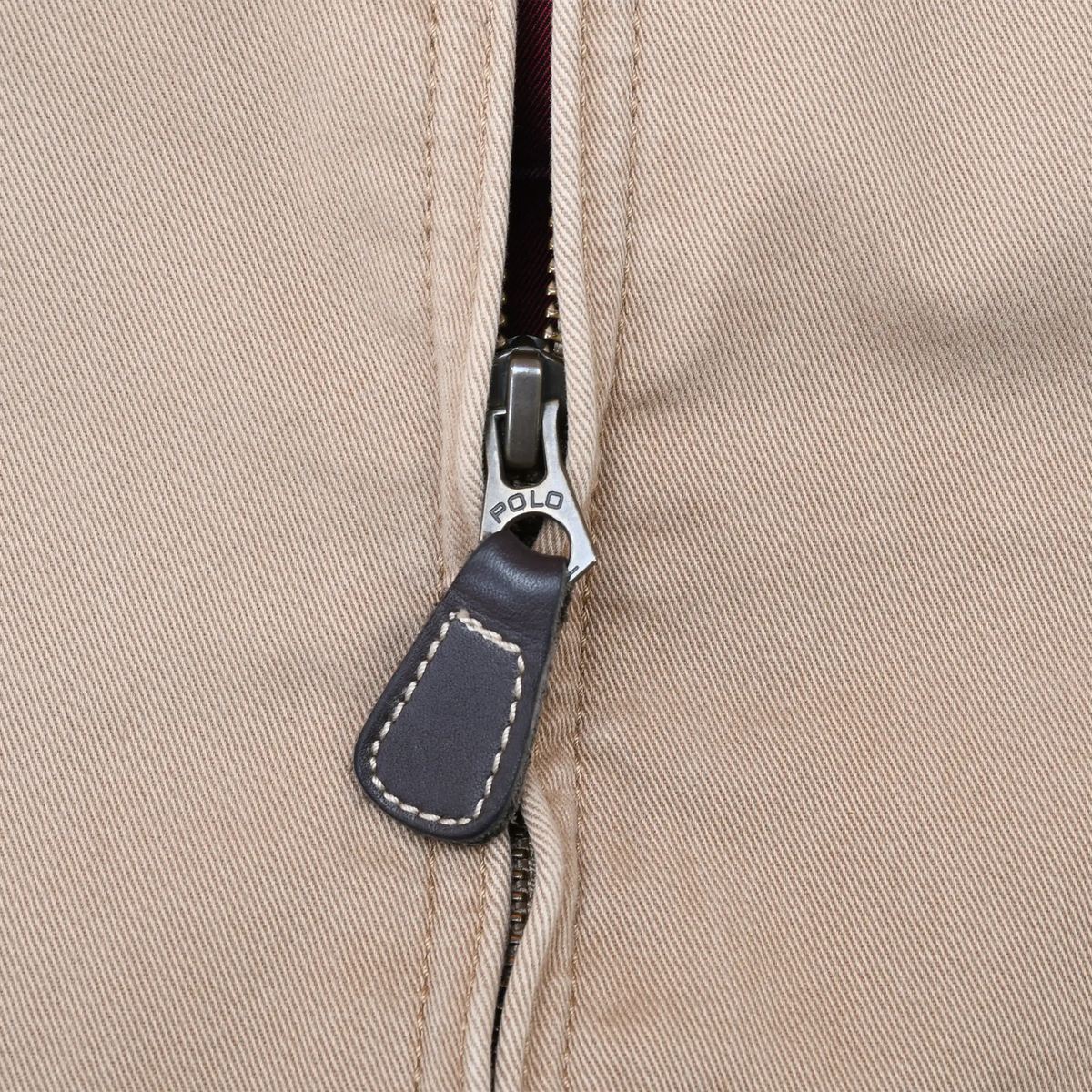 Close-up of Polo-engraved zipper and dark leather pull on brown jacket