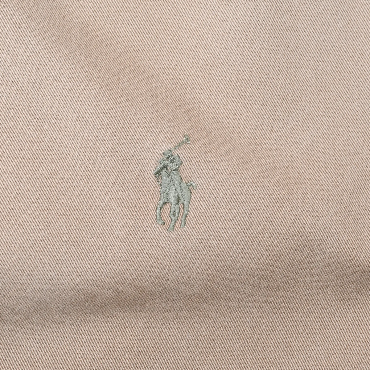 Close-up of green Polo pony embroidery on brown jacket fabric