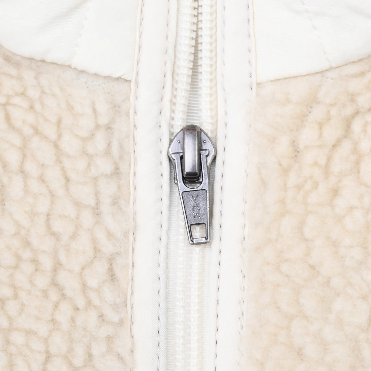 Close-up of metal zipper pull and white trim on beige fleece jacket