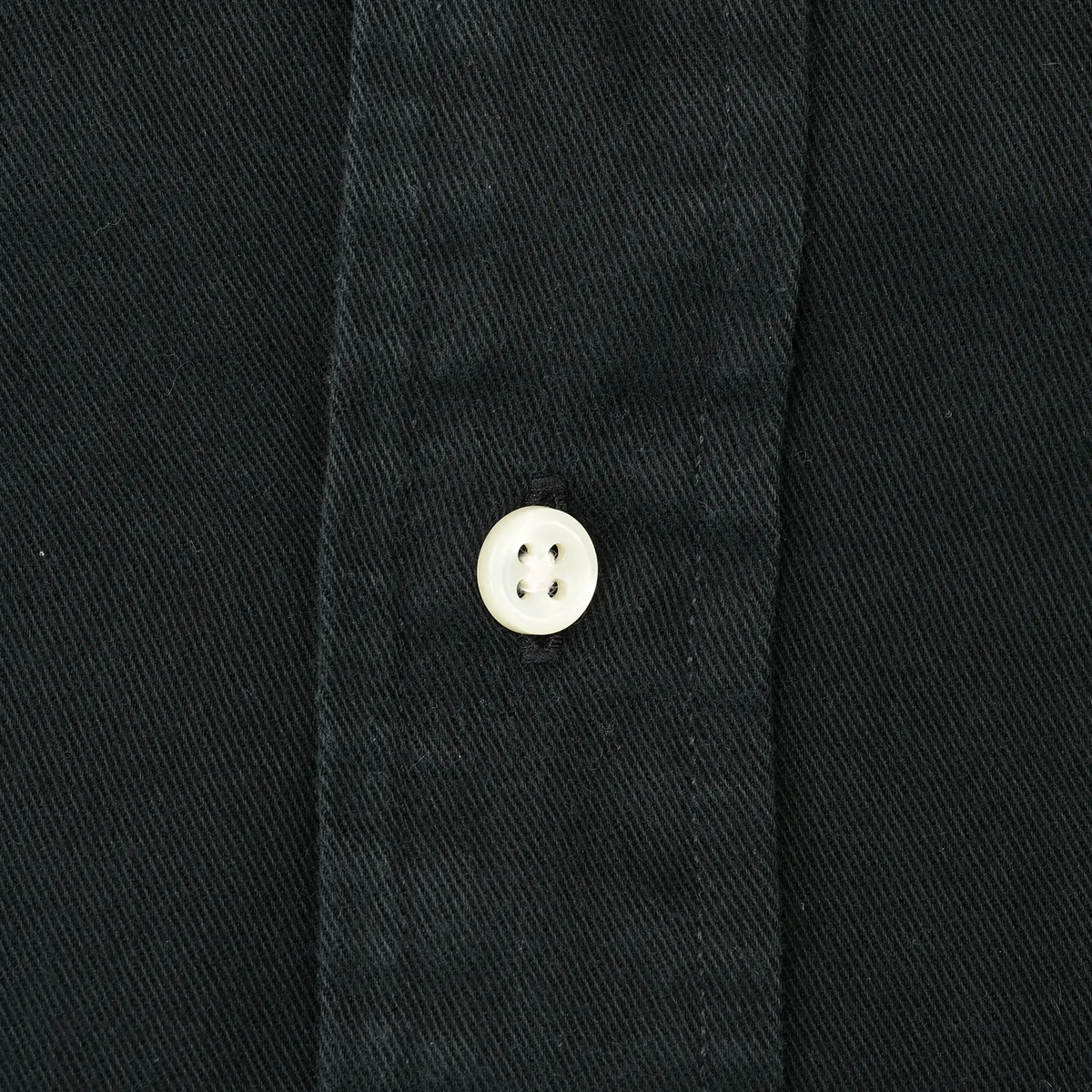 Close-up of white button and stitching on black shirt fabric