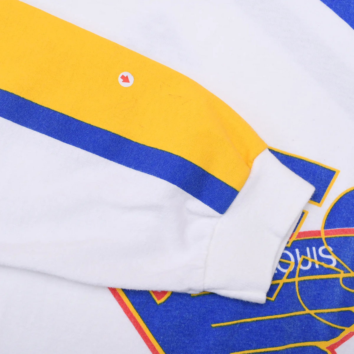 Sleeve detail with white cuff, yellow and blue stripes, and a small mark indicated by an arrow sticker