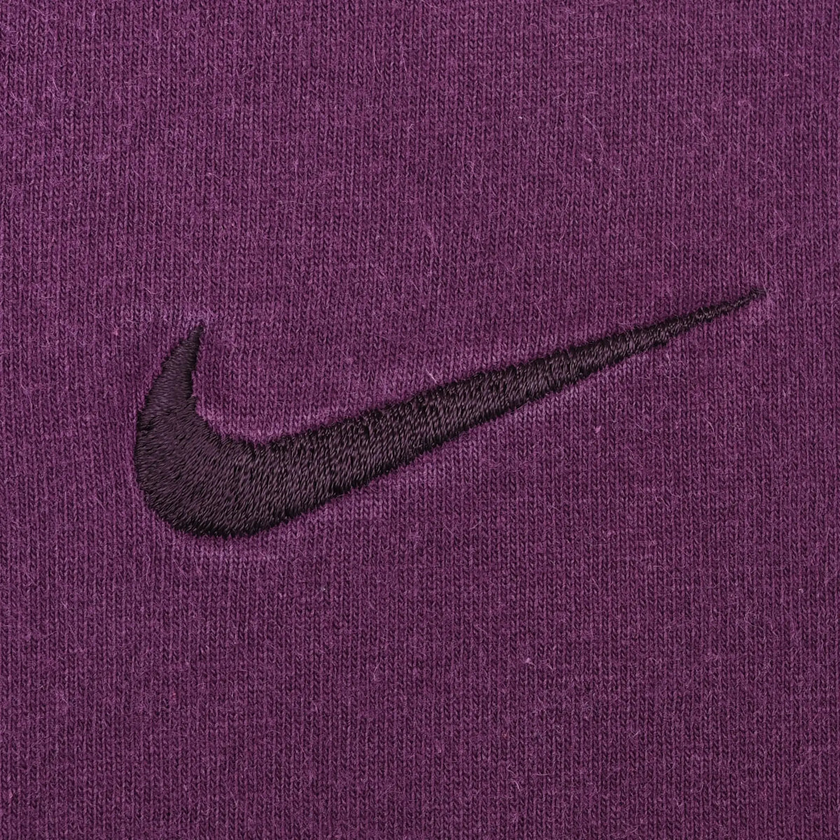 Close-up of dark Nike Swoosh embroidery on purple fabric