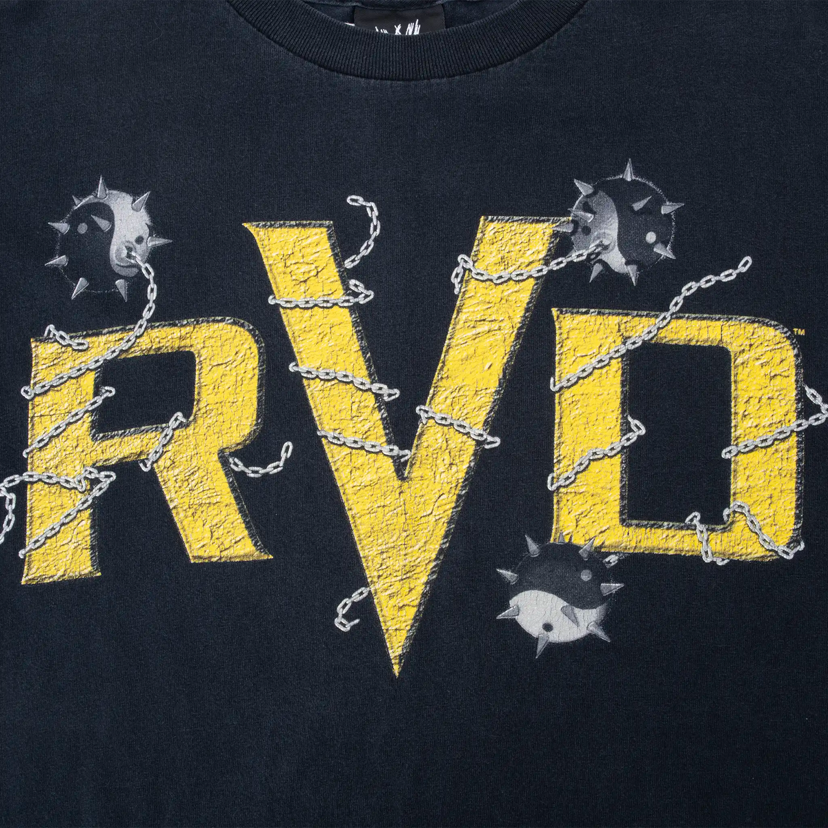 Close-up of yellow RVD front print with chains and spiked balls on black fabric