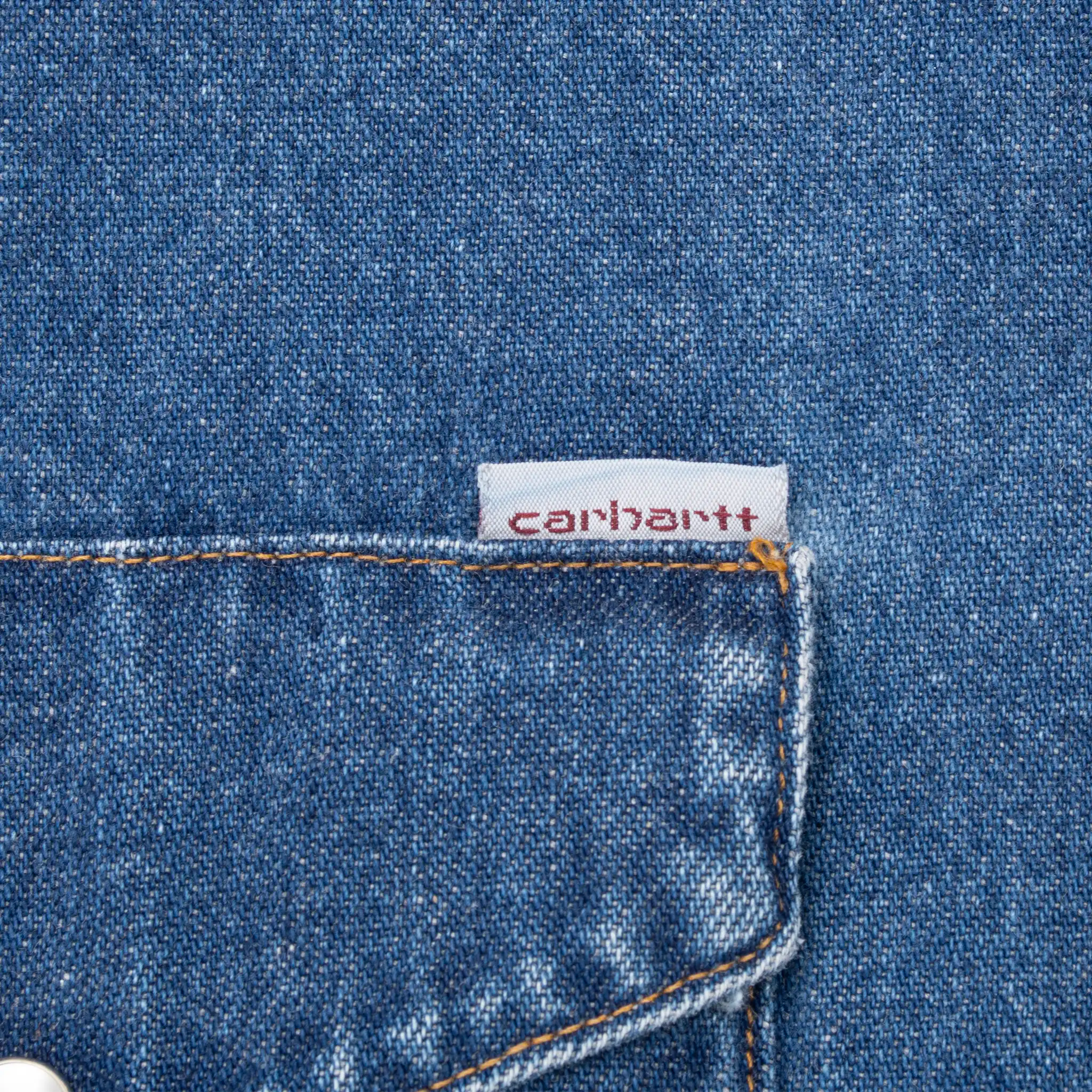 Close-up of Carhartt fabric tag above chest pocket on blue denim shirt