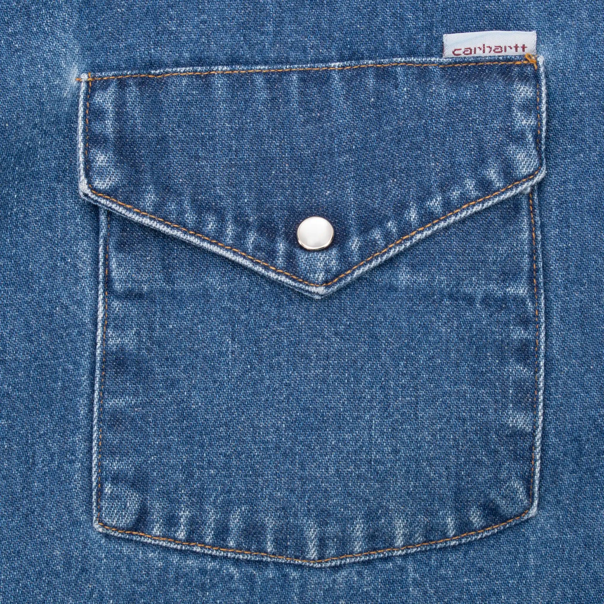 Blue denim chest pocket with pearl snap flap and Carhartt tag