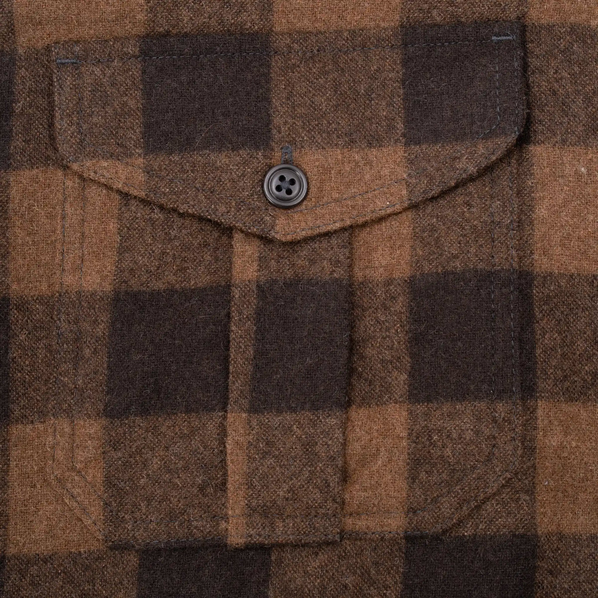 Close-up of buttoned chest pocket on brown and black plaid Filson shirt