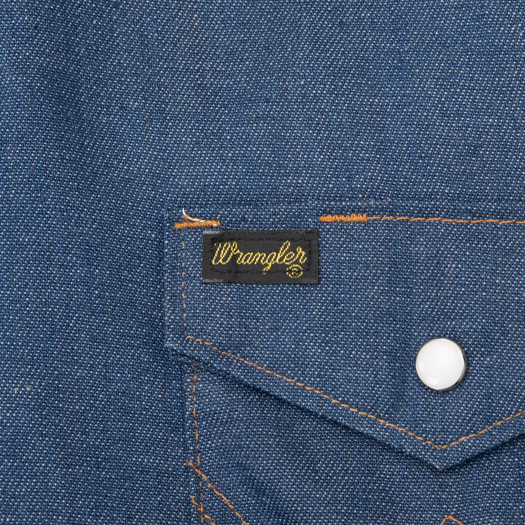 Close-up of Wrangler pocket tab, white pearl snap, and contrast stitching