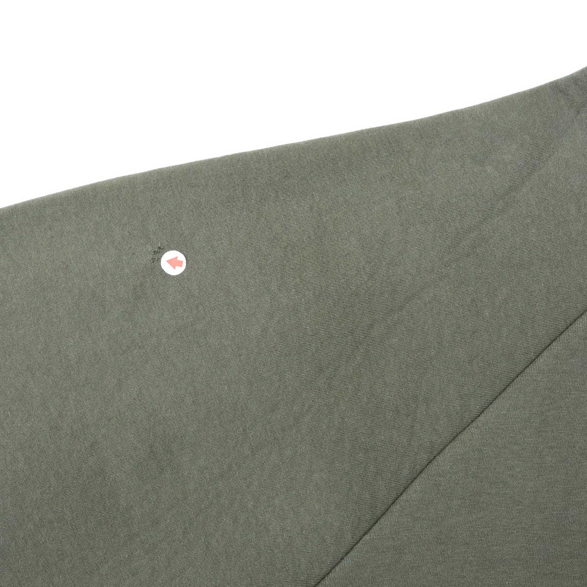 Close-up of olive green sleeve fabric with an arrow marking a small spot