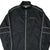 Close front view of black Nike windbreaker with orange chest embroidery, white piping, and zip pockets