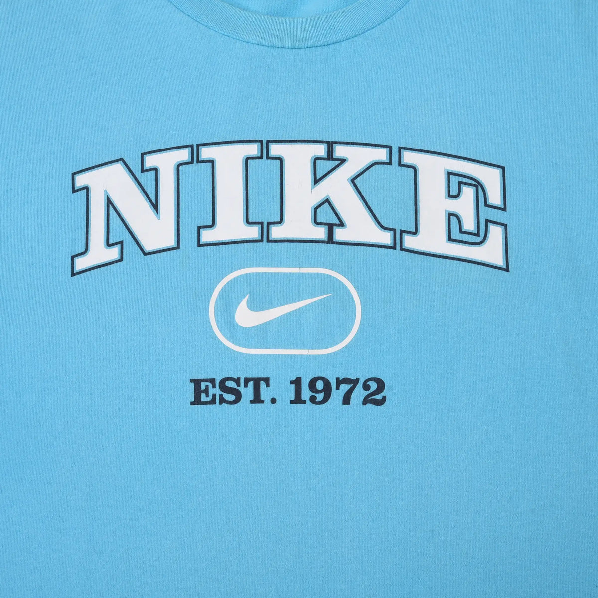 Close-up of white Nike spellout, Swoosh, and Est. 1972 print on light blue T-shirt