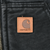 Close-up of tan Carhartt logo patch on faded black front pocket