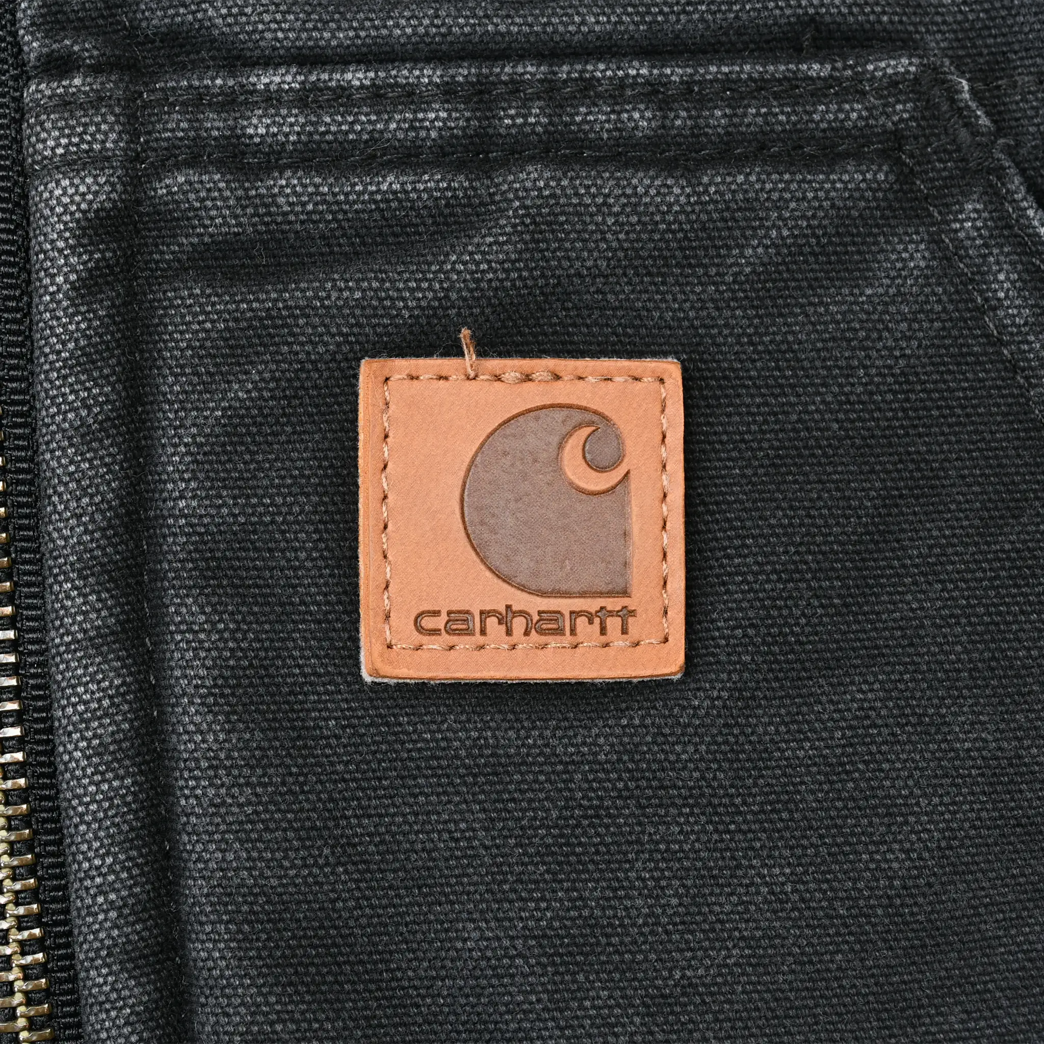 Close-up of tan Carhartt logo patch on faded black front pocket