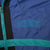 Close-up of teal Nike embroidery and stripe on blue windbreaker chest
