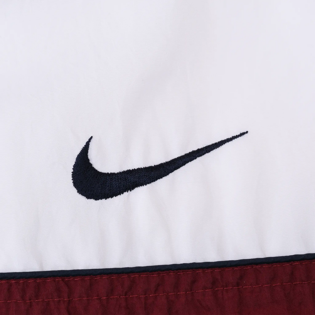 Close-up of navy Nike Swoosh embroidery on white chest panel