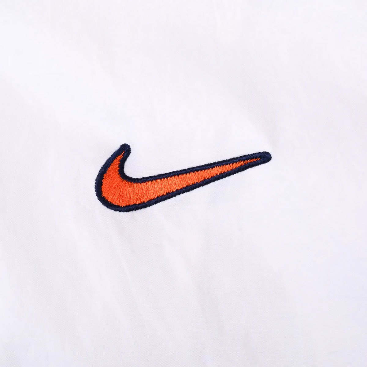 Close-up of small orange Nike Swoosh embroidery outlined in navy on white fabric