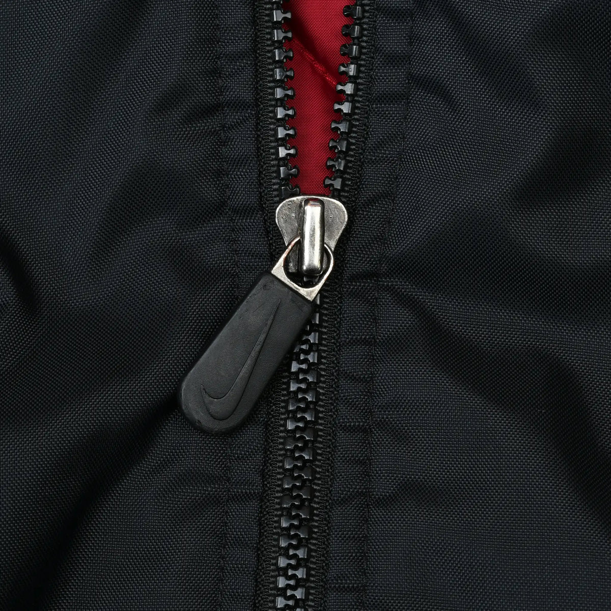 Close-up of black front zipper with Nike Swoosh pull and red lining