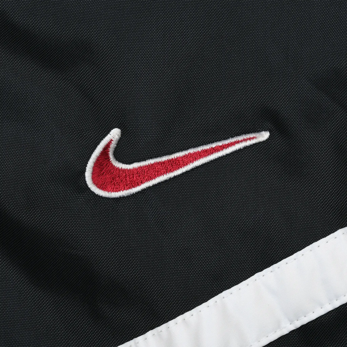 Close-up of red and white embroidered Nike Swoosh on black jacket shell