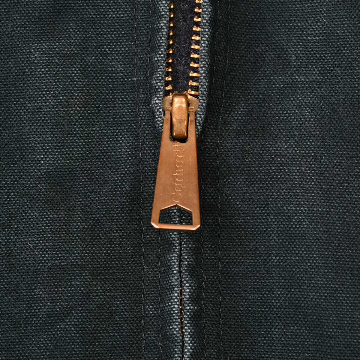 Close-up of brass-tone Carhartt zipper pull on black jacket fabric