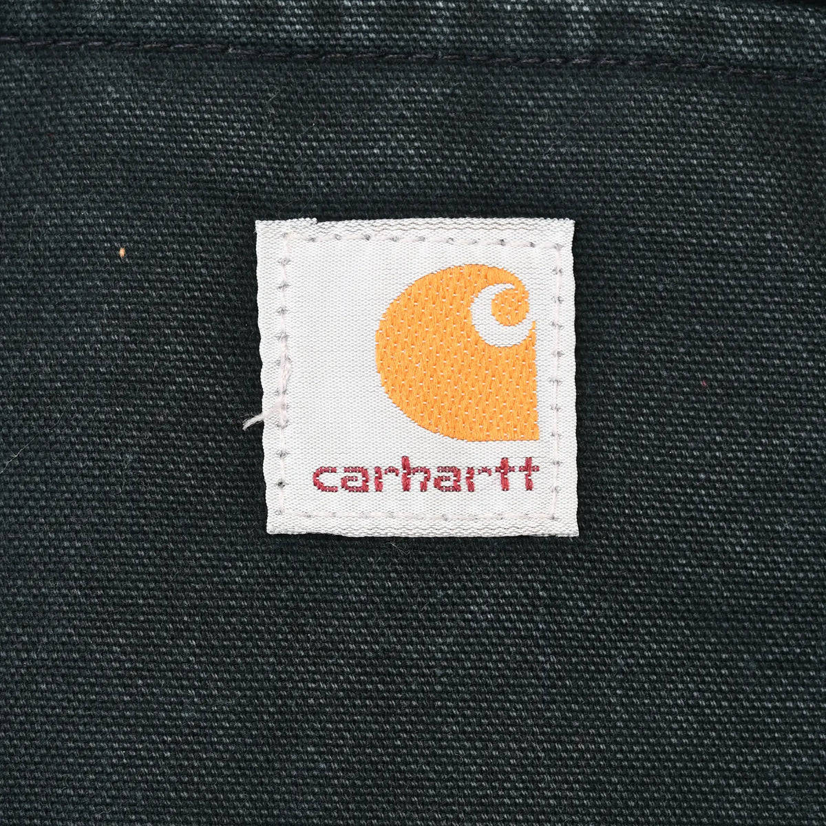 Close-up of square Carhartt logo patch stitched on black jacket fabric
