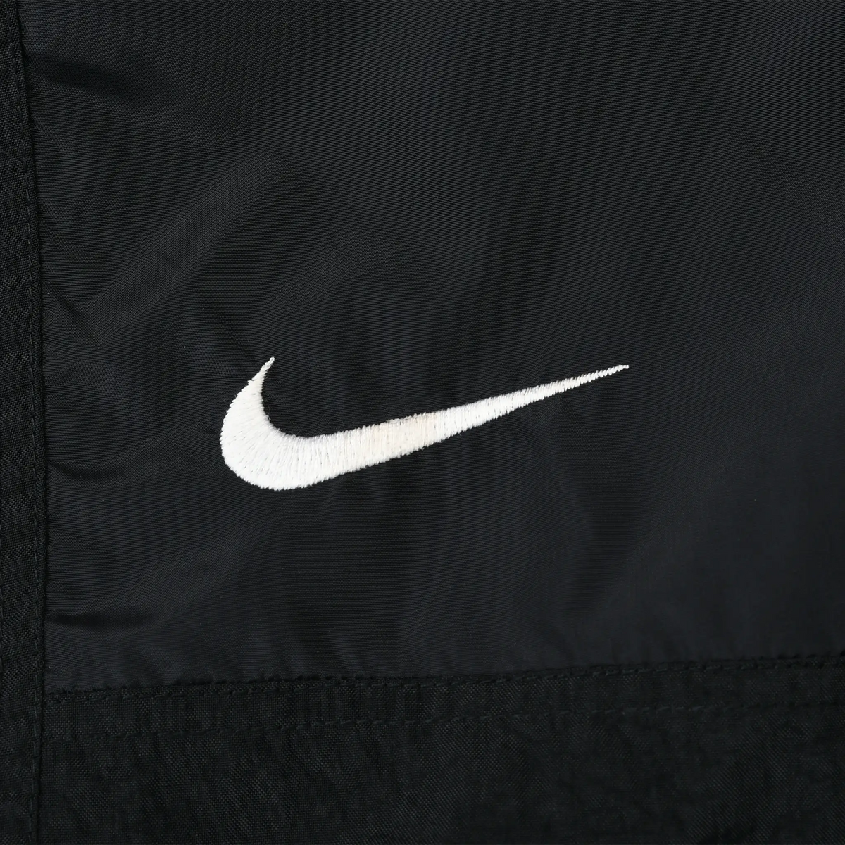Close-up of white Nike Swoosh embroidery on black jacket front